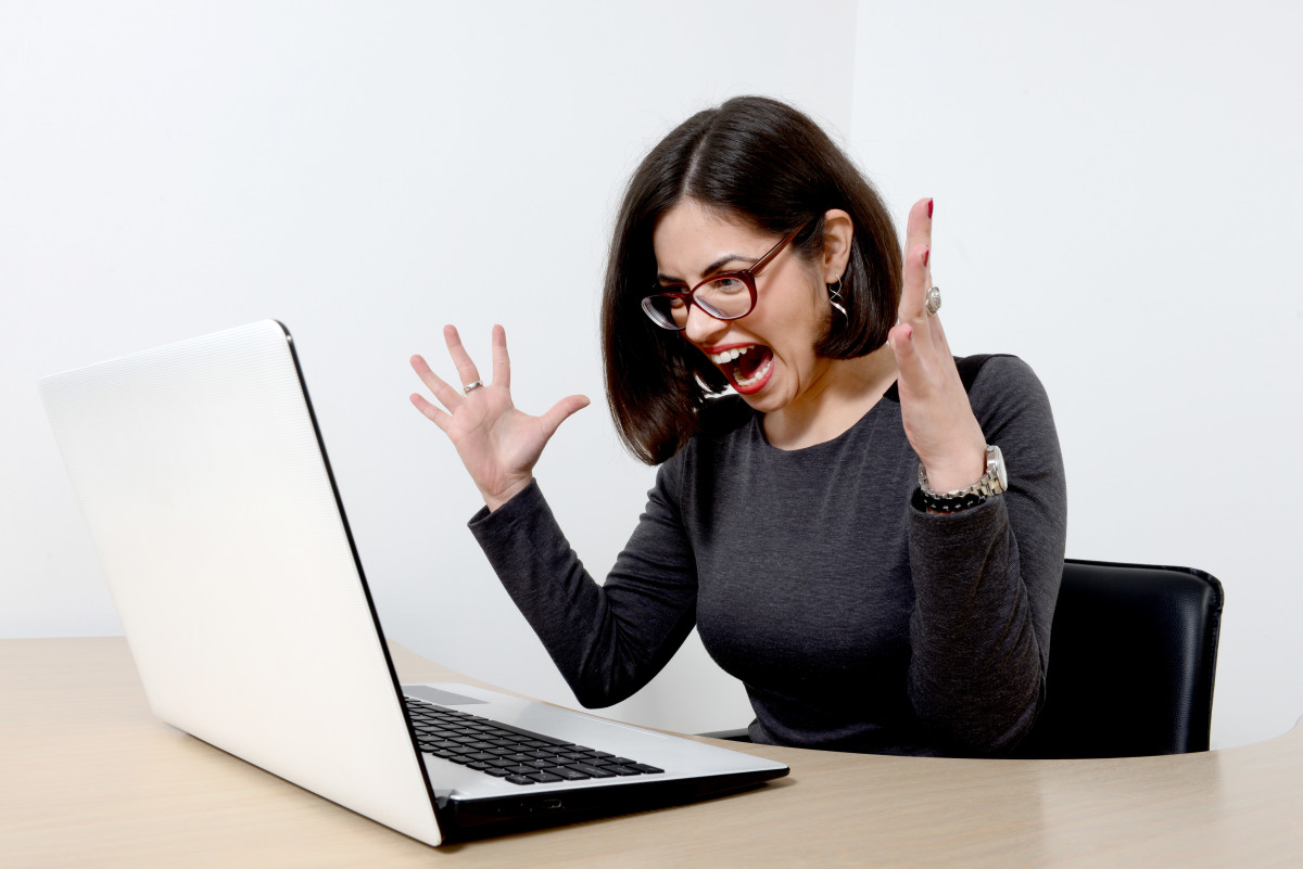 Young beautiful stressed businesswoman screaming at laptop.